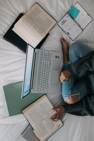 image of person on bed with laptop and books