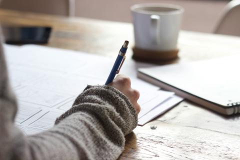 phot of hand holding pen, desk with paper and mug